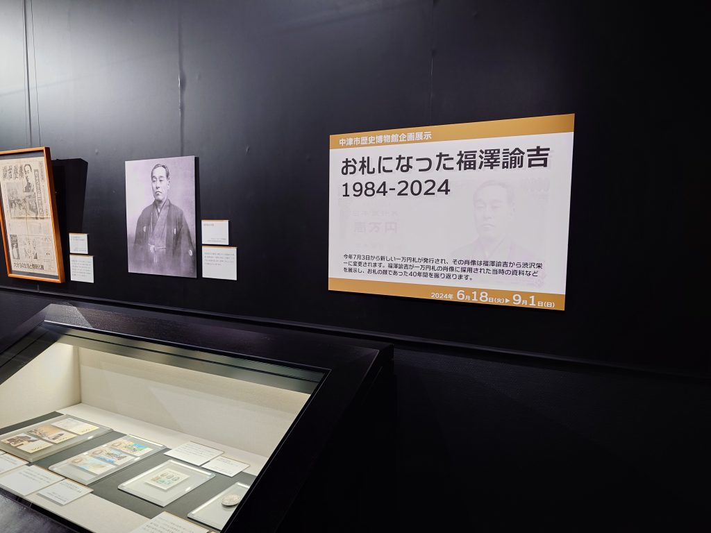 お札になった福澤諭吉展、展示の様子を写した写真。タイトル看板や肖像が壁面に、壁沿い設置のケースには1984年当時の記念品が展示されている。